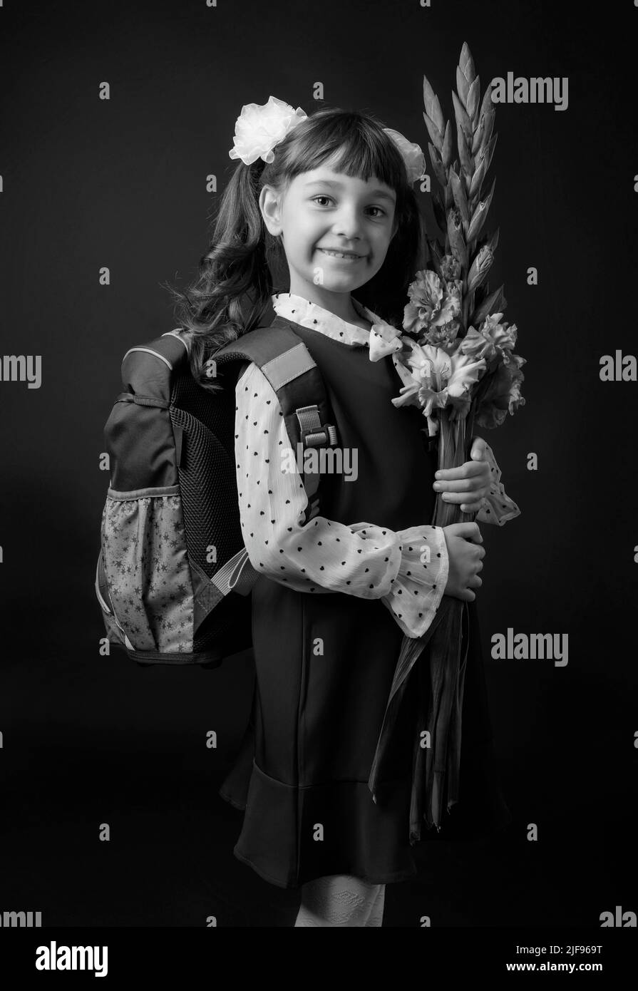 Portrait d'une fille dans un uniforme d'école primaire. Un haut-grader avec un sac à dos et des fleurs. Noir et blanc. Banque D'Images