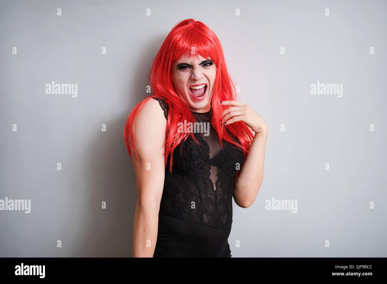 Portrait d'une reine de drag criant et portant une perruque rouge sur fond gris. Banque D'Images