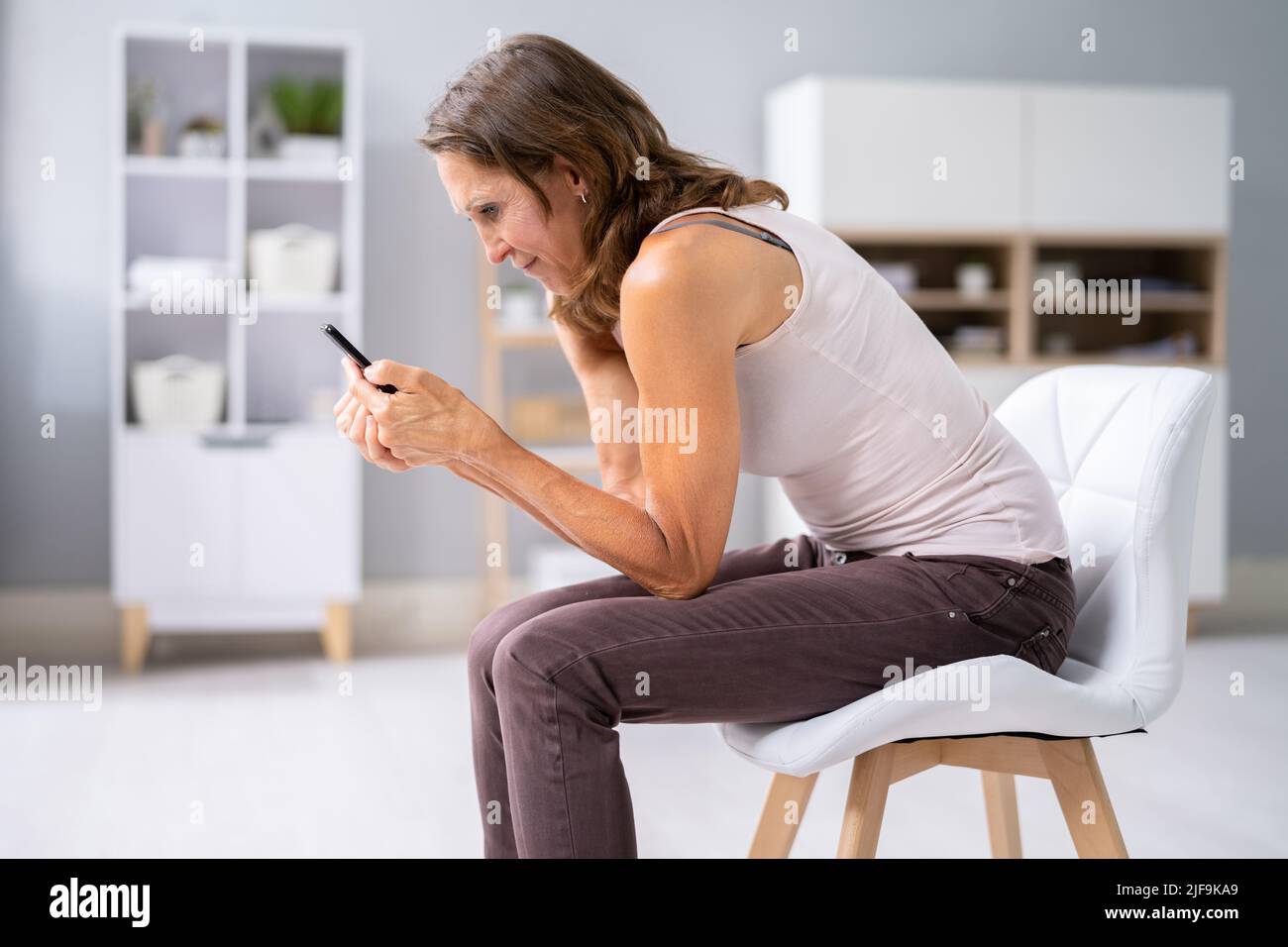 Femme souffrant de douleurs au cou assis à l'aide d'un téléphone portable Banque D'Images