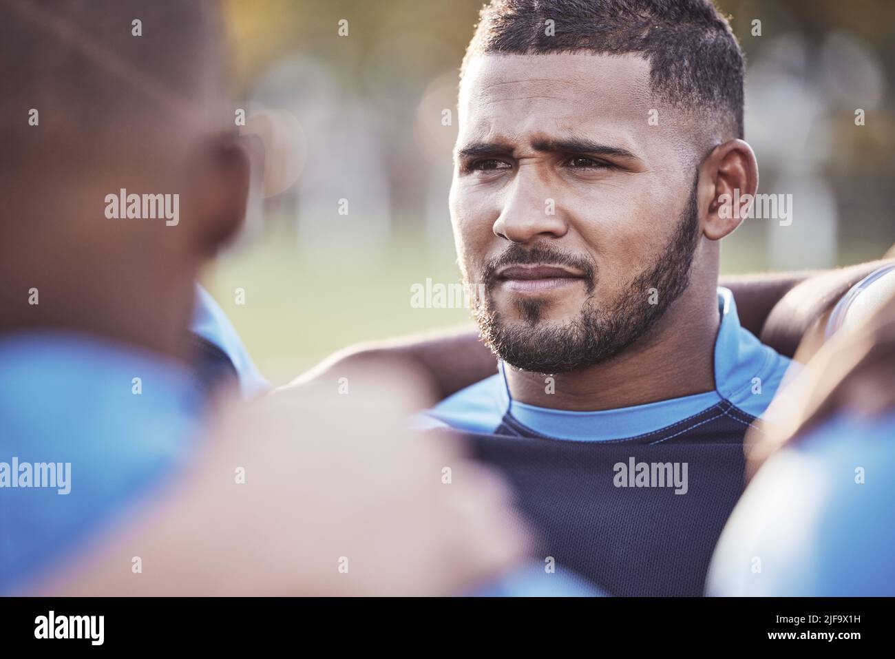 Gros plan joueur de rugby de course mixte debout dans un caucus avec ses coéquipiers à l'extérieur sur un terrain. Athlète hispanique masculine qui a l'air sérieuse et concentrée pendant Banque D'Images