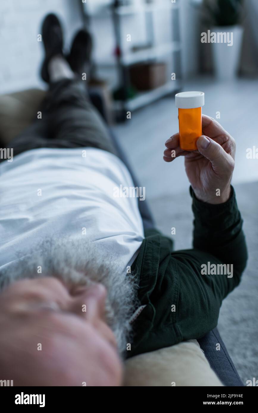 homme sénior flou tenant une bouteille avec un médicament anti-dépresseur tout en étant allongé sur un canapé dans la salle de séjour Banque D'Images