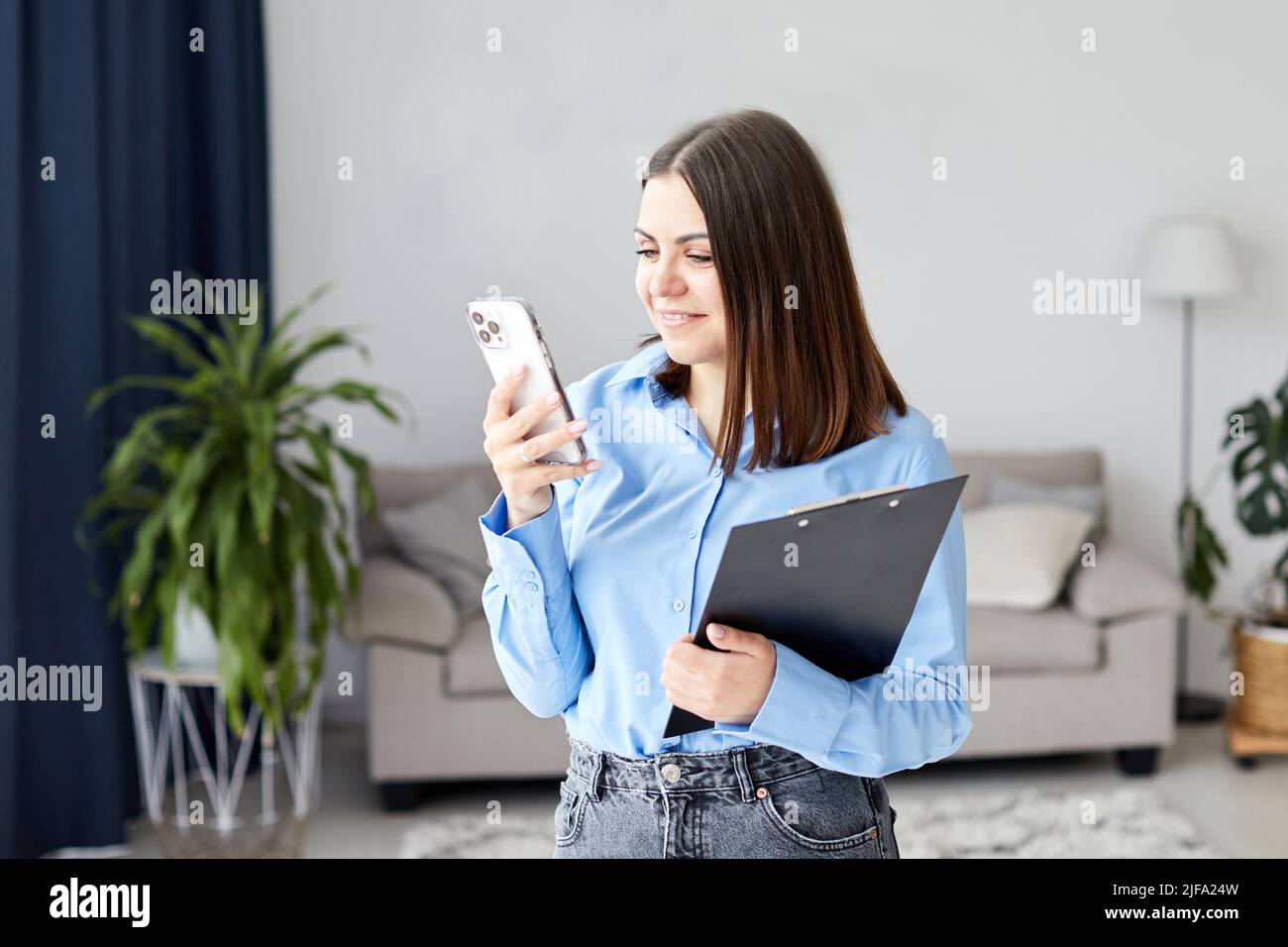 Une jeune femme bavarde au téléphone et souriante, debout au milieu de la pièce, a reçu un message de la famille, parlant par vidéo, relation longue distance Banque D'Images