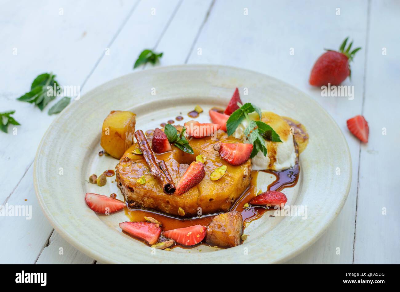 Tranche d'ananas caramélisée avec crème glacée, fraises, pistaches, menthe et bâton de cannelle Banque D'Images