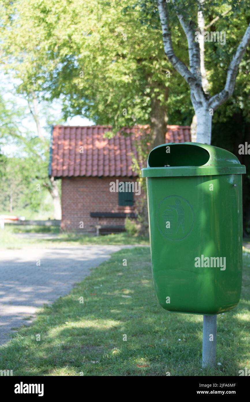 vider la poubelle verte à herbe ou la poubelle avec un pictogramme à côté d'un chemin avec un bouleau et une petite maison en briques à l'arrière Banque D'Images