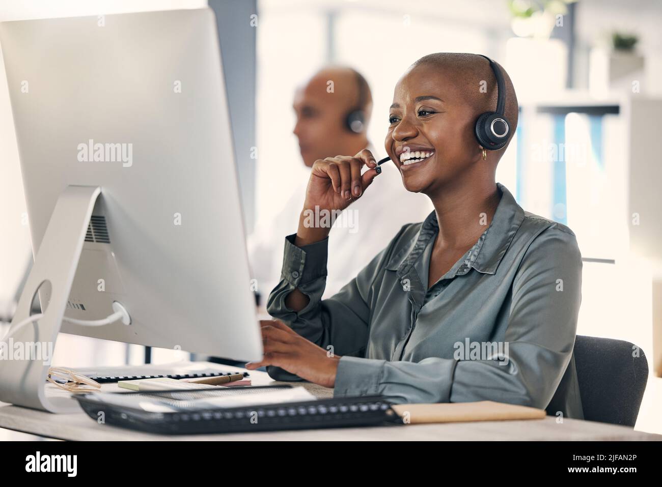 Un jeune agent de télémarketing de centre d'appels afro-américain satisfait parlant sur un micro-casque tout en travaillant sur un ordinateur dans un bureau. Femme confiante et amicale Banque D'Images