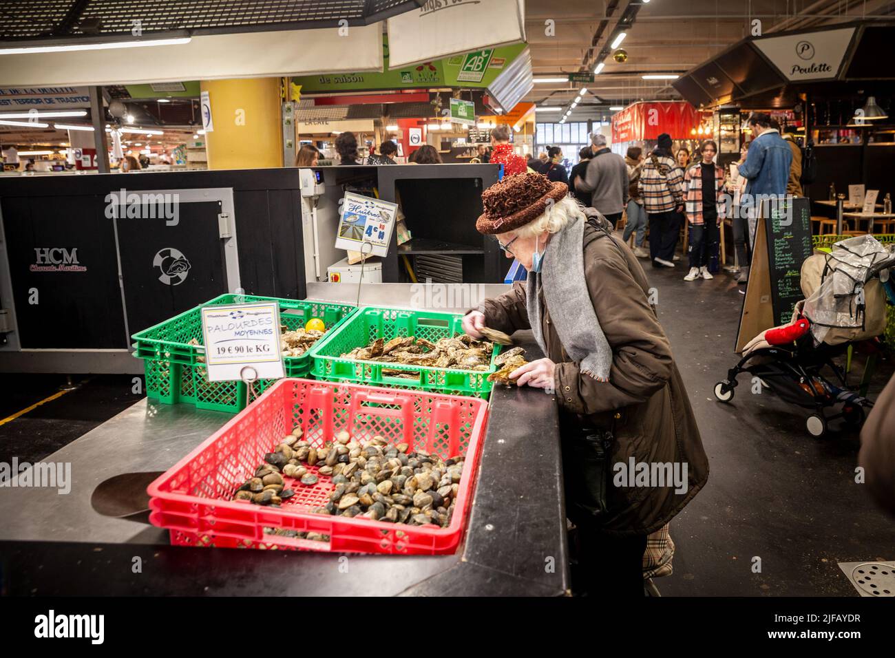 Photo d'une vieille femme sur le marché des Capucins à Bordeaux, à la recherche d'huîtres et d'autres coquillages de fruits de mer, à vendre sur un stand. Les huîtres sont Banque D'Images
