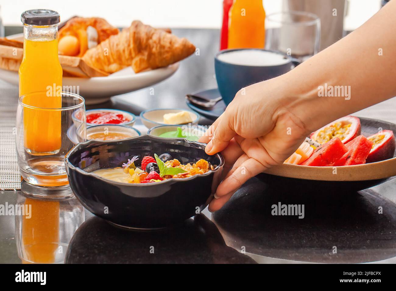 Nourriture végétalienne saine dans le café. Femme main place une assiette avec bol à smoothie sur la table. Nourriture biologique le matin, fruits frais, jus, latte sans lactose Banque D'Images