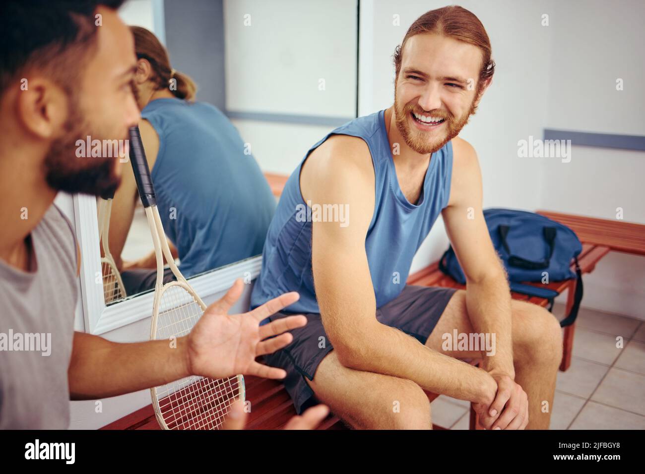 Des amis joyeux qui parlent dans la salle de gym. Les joueurs heureux se sont encollants et parlent dans un vestiaire. Les hommes parlent et se détendent avant un match. Deux athlètes assis Banque D'Images