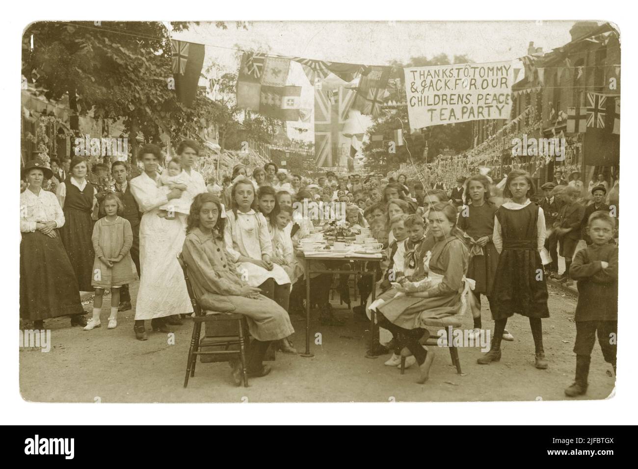 Carte postale originale datant de l'époque WW1 d'un groupe d'enfants assis à des tables à l'extérieur de la rue pour une partie de la paix qui célèbre la fin de la guerre mondiale de 1st - la bannière se lit comme suit : « Merci à Tommy & Jack for Our Childrens Peace Tea », Boston Rd., Walthamstow London, R.-U. daté de 1918 Banque D'Images