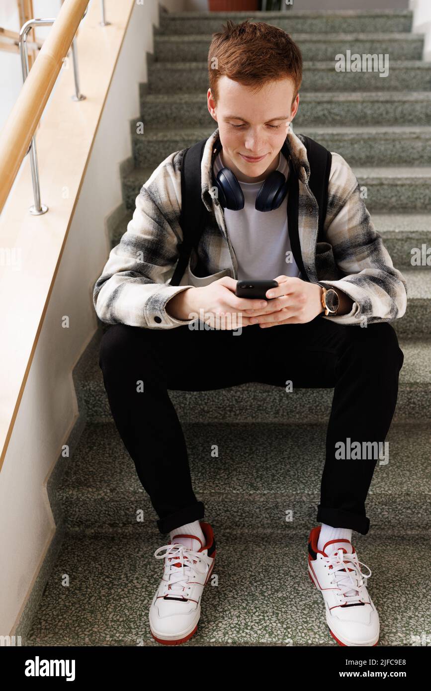 Étudiant assis dans un escalier et utilisant un smartphone Banque D'Images