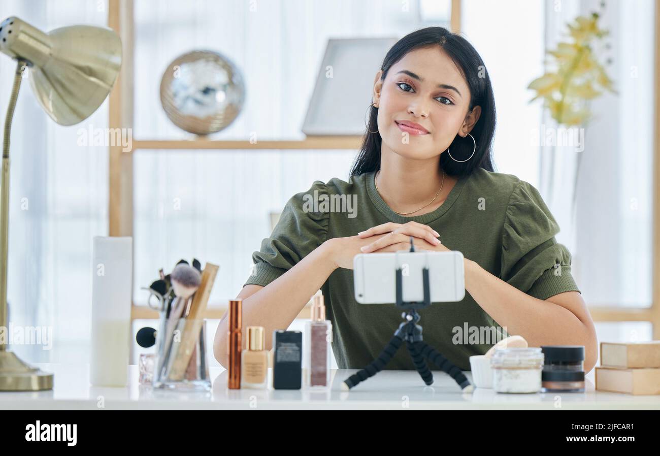 Portrait de la beauté blogueuse souriant tout en étant assis avec son smartphone et en faisant un tutoriel de maquillage. Belle jeune influenceur partageant sa beauté Banque D'Images
