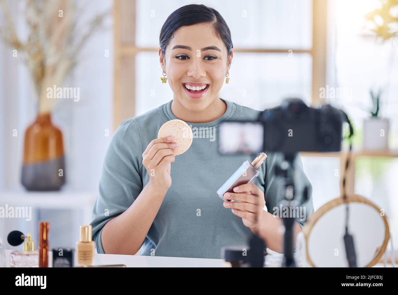 Joyeux jeune blogueur de beauté tenant un produit de beauté et une éponge tout en faisant un tutoriel de maquillage et d'enregistrement avec son trépied. Influenceur travaillant en tant que Banque D'Images