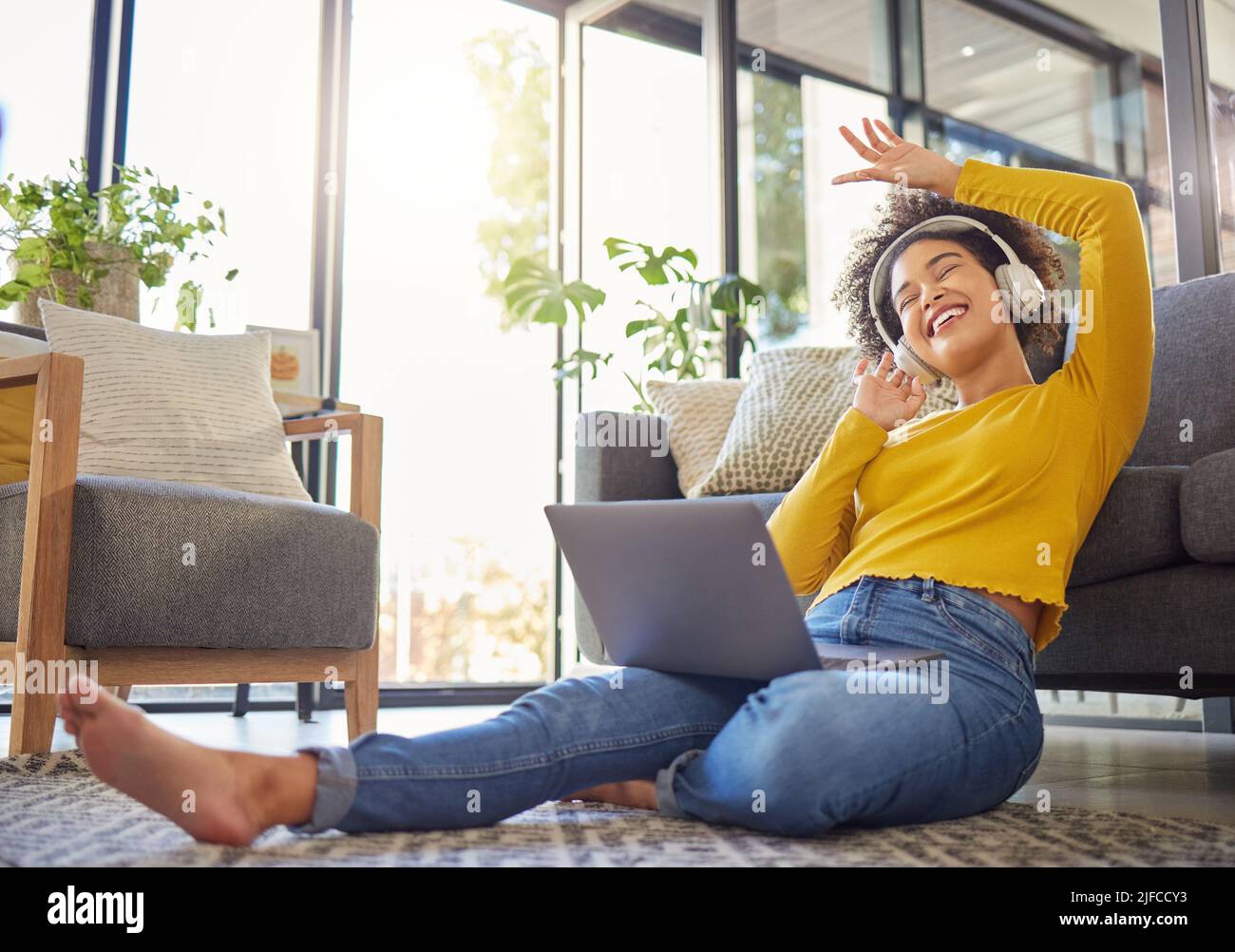 Jeune femme joyeuse de course mixte portant des écouteurs et écoutant de la musique tout en utilisant un ordinateur portable à la maison. Une femme hispanique gaie avec une frino curieuse Banque D'Images