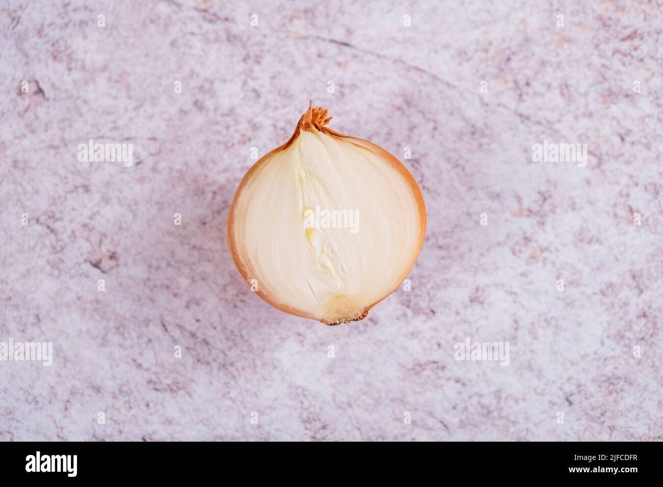 Un oignon blanc divisé en deux avec la peau, sur un fond de surface en pierre blanche. Banque D'Images