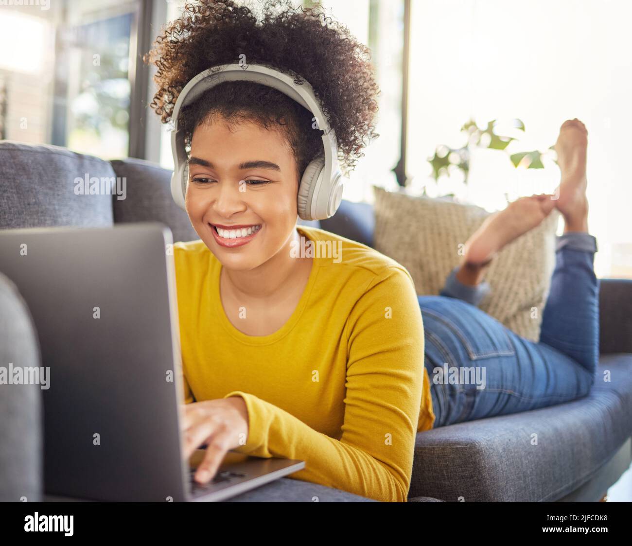 Jeune femme joyeuse de course mixte portant des écouteurs et écoutant de la musique tout en utilisant un ordinateur portable à la maison. Une heureuse femme hispanique avec une frino mauriquement Banque D'Images