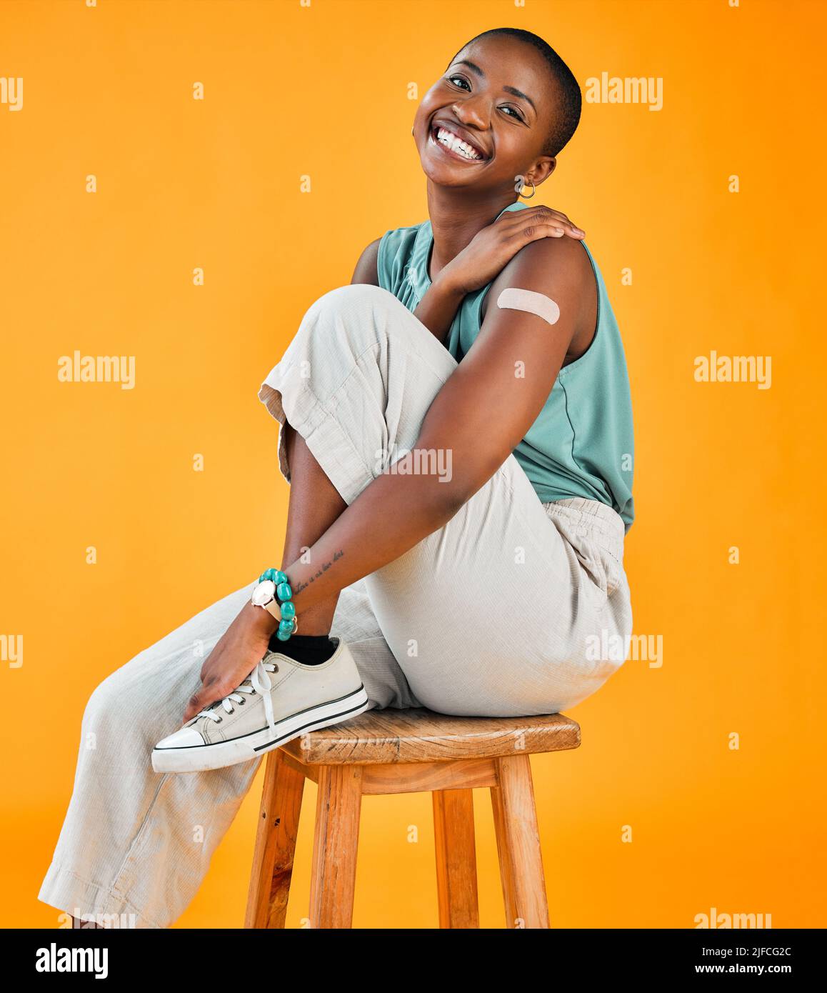 Femme vaccinée Covid afro-américaine montrant du plâtre sur le bras et souriant. Portrait de modèle noir isolé sur fond jaune studio avec Banque D'Images