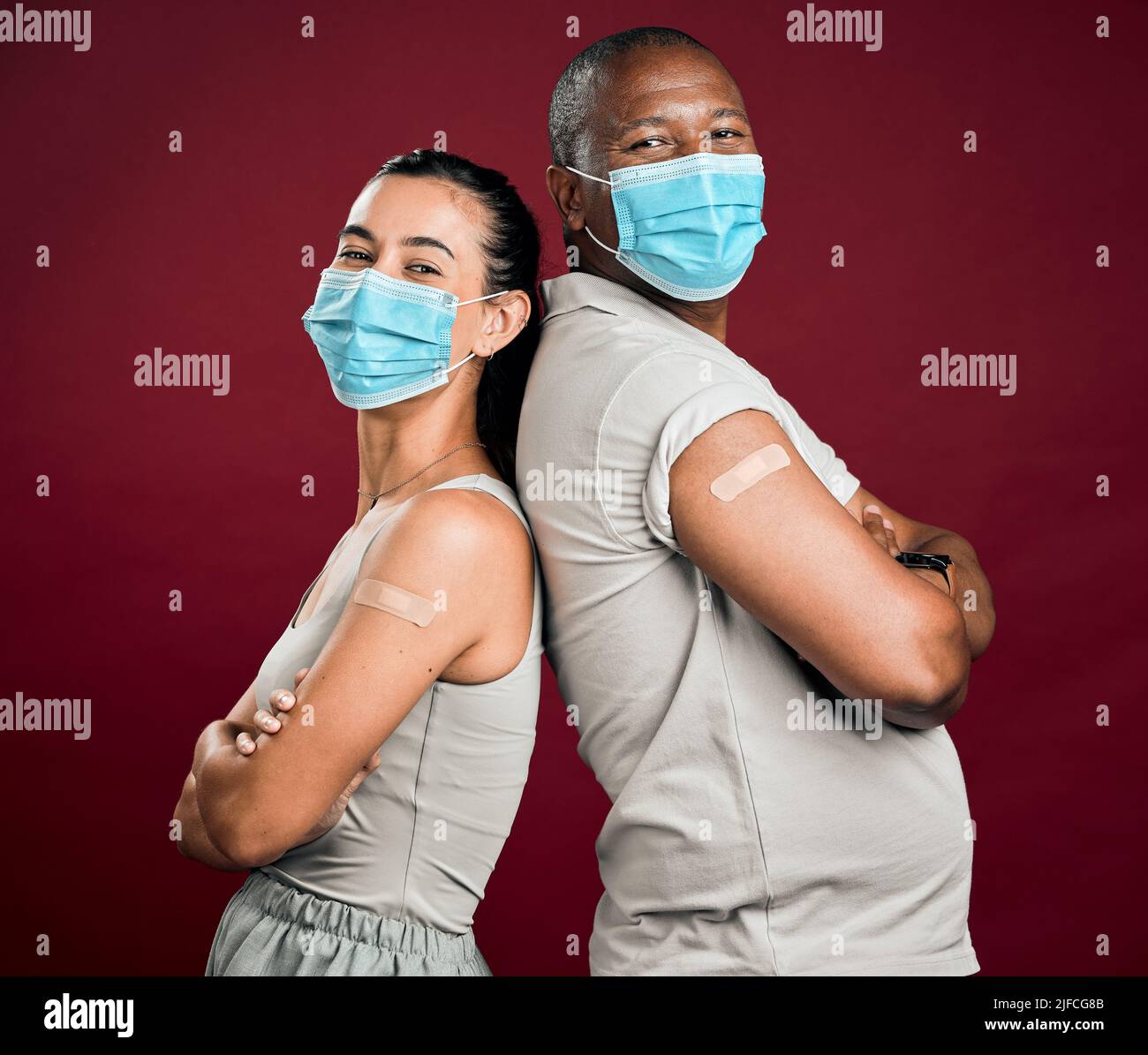Covid a vacciné un homme afro-américain et une femme de race mixte se tenant dos à dos. Deux personnes portant un masque chirurgical isolé du rouge Banque D'Images
