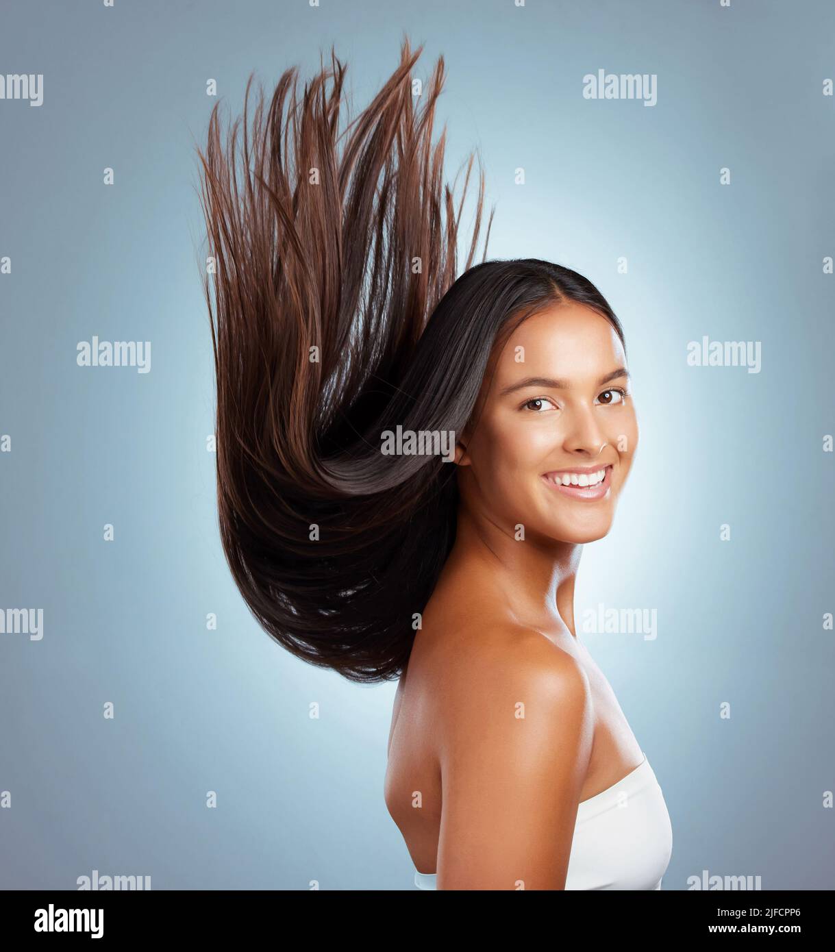 Portrait d'une femme hispanique brunette avec de longs cheveux luxuriants et beaux souriant et posant sur un fond gris studio. Race mixte femelle debout Banque D'Images