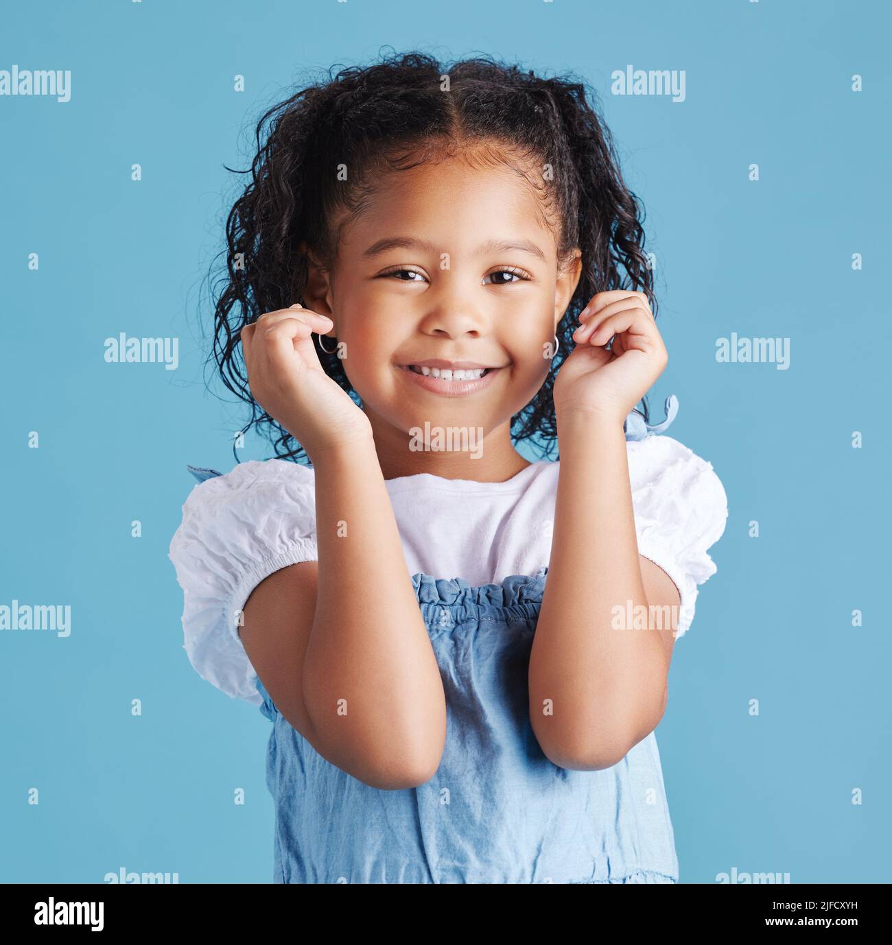 Portrait d'une petite fille aux cheveux bruns souriante posant avec ses mains vers le haut montrant des coudes. Joyeux enfant avec de bonnes dents saines pour les dents sur fond bleu Banque D'Images