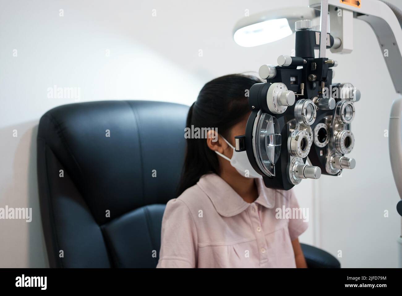 Ophtalmologiste examinant les yeux d'une fille asiatique dans une clinique. Ils portent des masques de protection. Banque D'Images