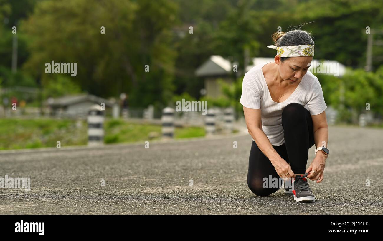 Femme d'âge moyen nouant des lacets, se préparer pour le jogging en plein air. Concept de mode de vie sain Banque D'Images