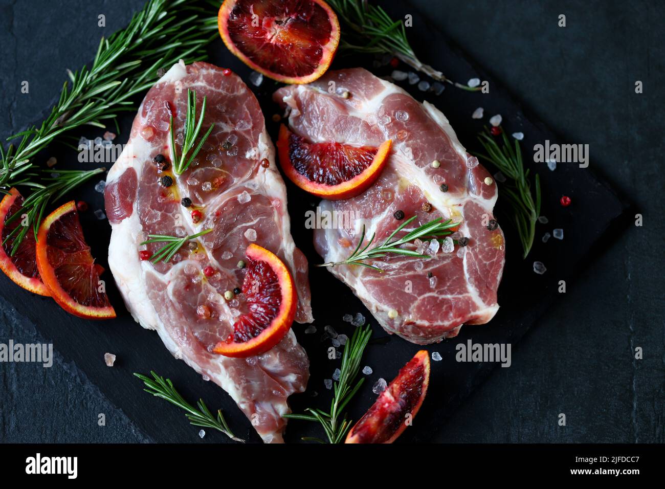 Steaks de porc crus marinés au romarin et à l'orange sur un panneau de pierre. Cuisson de steaks de viande. Banque D'Images