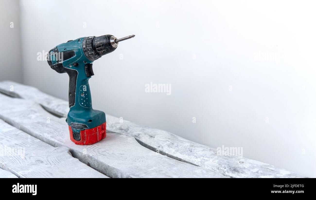 Un tournevis électrique se tient sur un support en bois blanc à partir de planches près d'un mur blanc. Travaux de construction à domicile. Réparation à l'atelier de bricolage Banque D'Images
