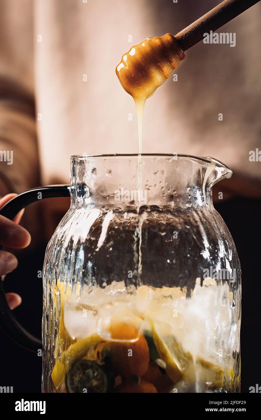 Ajouter du miel aux agrumes réfrigérés dans des bocaux en verre, frais et fruité boisson froide processus de fabrication - photo de stock Banque D'Images