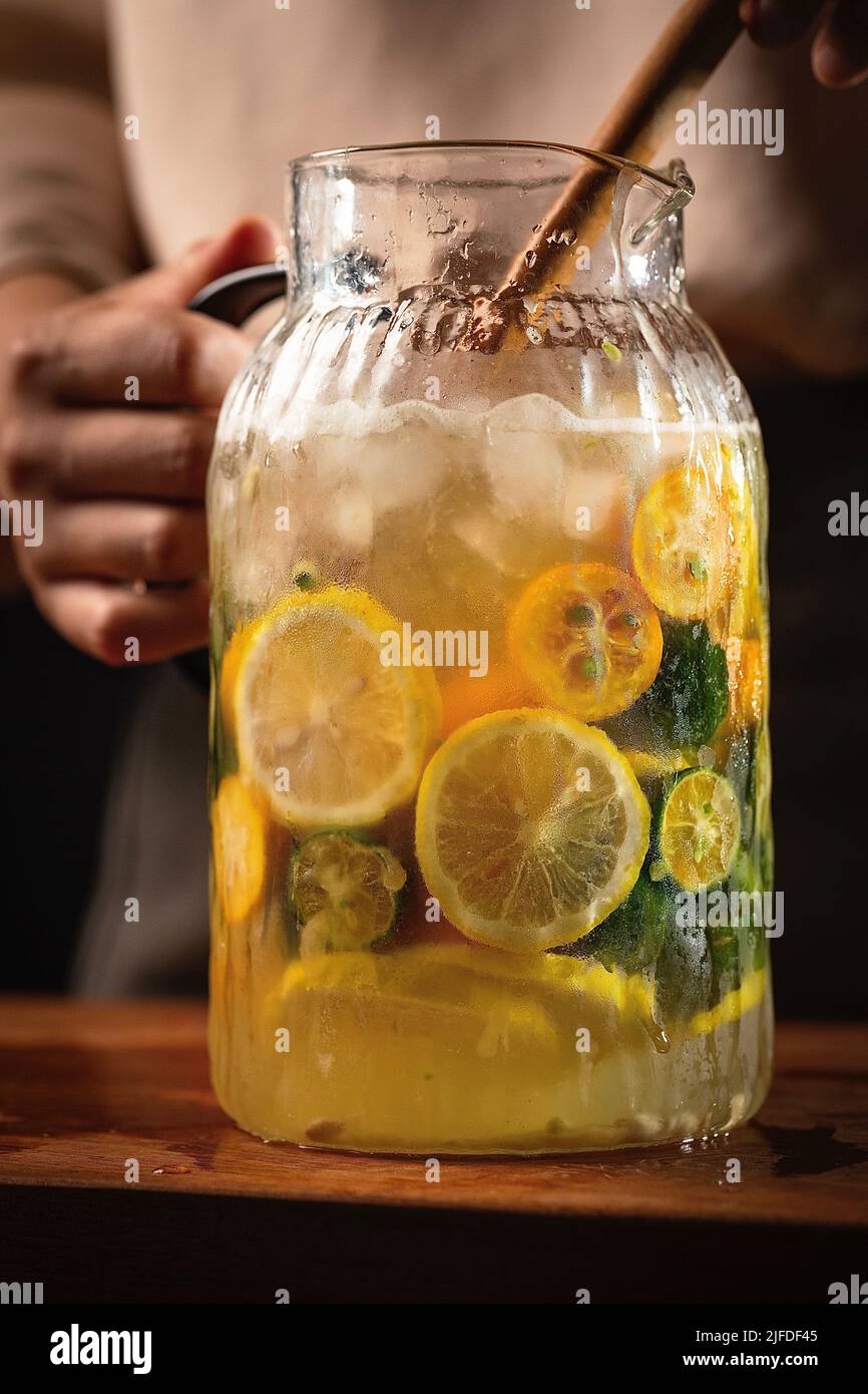 En remuant le mélange d'agrumes frais dans un pot en verre, le processus de fabrication de boisson froide fraîche et fruitée - photo de stock Banque D'Images