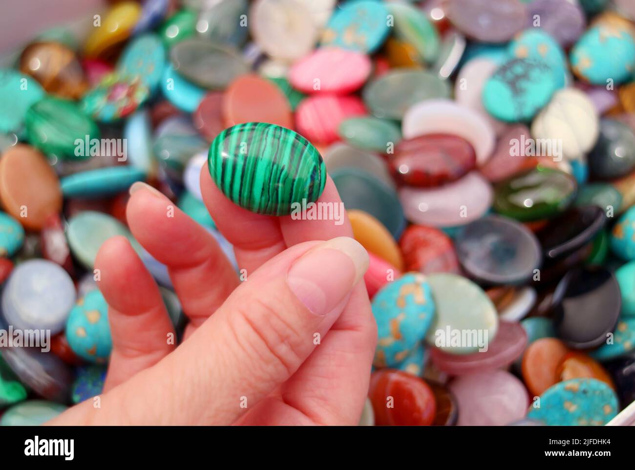Gros plan de la main de la femme cueillant une pierre malachite avec des pierres semi-précieuses floues pile en arrière-plan Banque D'Images