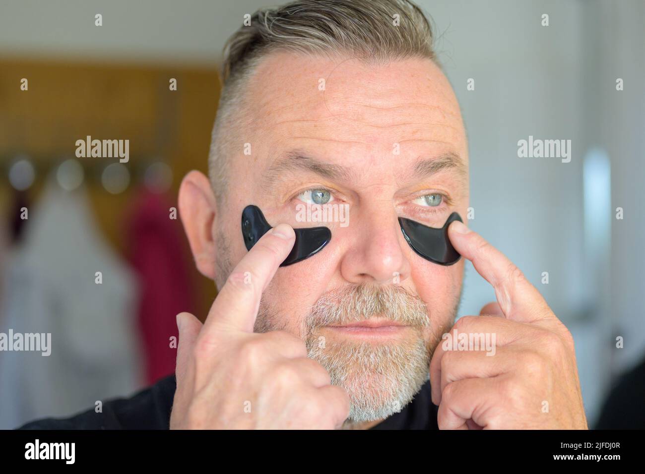 Homme d'âge moyen appliquant des plaques d'hydratation en gel des yeux du bout des doigts dans un concept de soins de la peau Banque D'Images