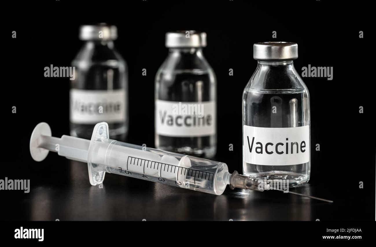 Trois flacons de vaccin en verre sur carton noir, seringue hypodermique près Banque D'Images