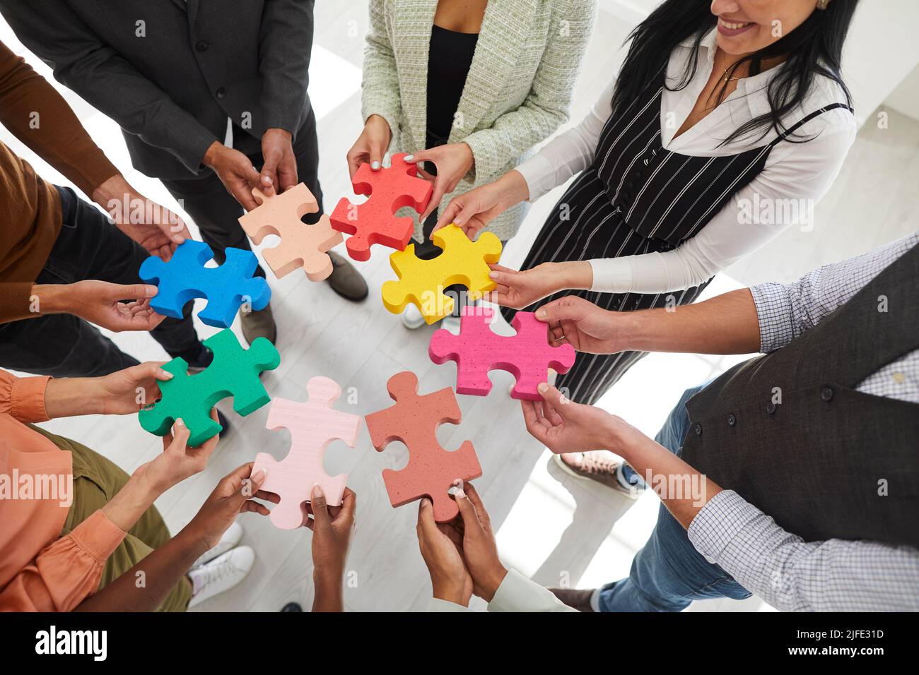 Image rognée d'un groupe d'hommes et de femmes se tenant dans un cercle et reliant des pièces de puzzle de couleur. Banque D'Images