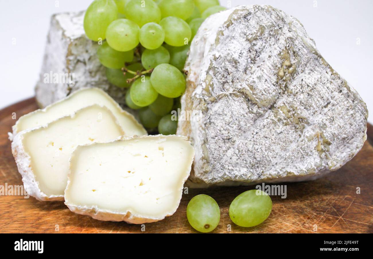 Assortiment de fromages bleu moldy lait de chèvre sur une planche à découper en bois avec des raisins verts. Arrière-plan blanc. Banque D'Images