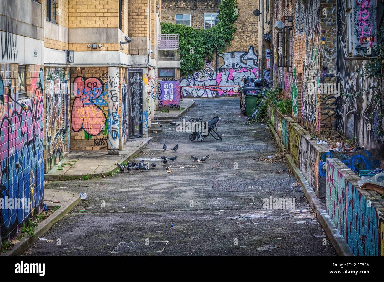 Des graffitis couvraient les murs avec une poussette retournée dans une rue à l'arrière de Brick Lane à Londres. Banque D'Images