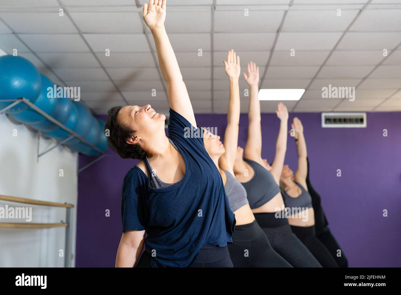 Gros plan d'un groupe souriant de femmes pratiquant le guerrier une pose sur la classe de yoga Banque D'Images