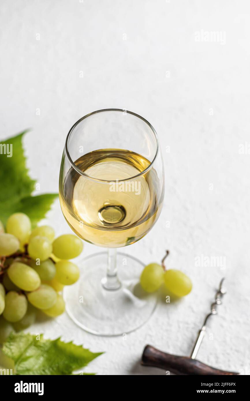 Verre de vin blanc avec raisins et tire-bouchon sur fond blanc avec espace de texte. Orientation verticale Banque D'Images