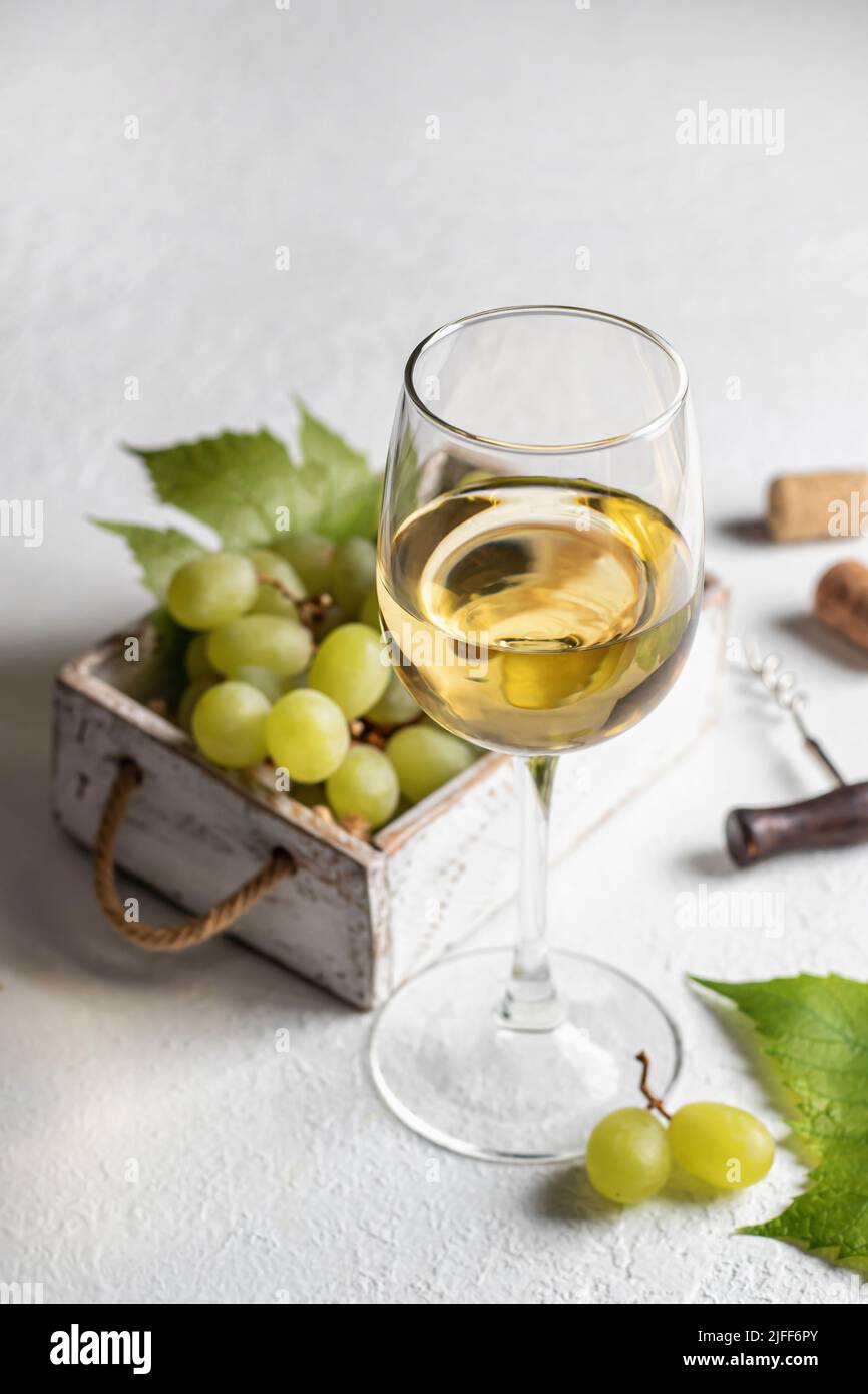 Verre de vin blanc avec raisins, corks et tire-bouchon sur fond de table blanc avec espace de texte. Orientation verticale Banque D'Images