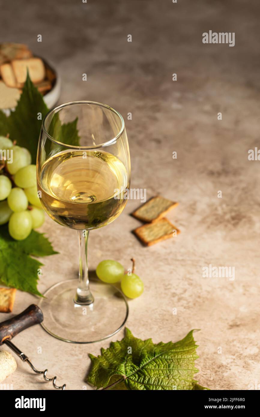 Verre de vin blanc avec raisins et tire-bouchon et craquelins sur fond marron avec espace de texte. Orientation verticale Banque D'Images
