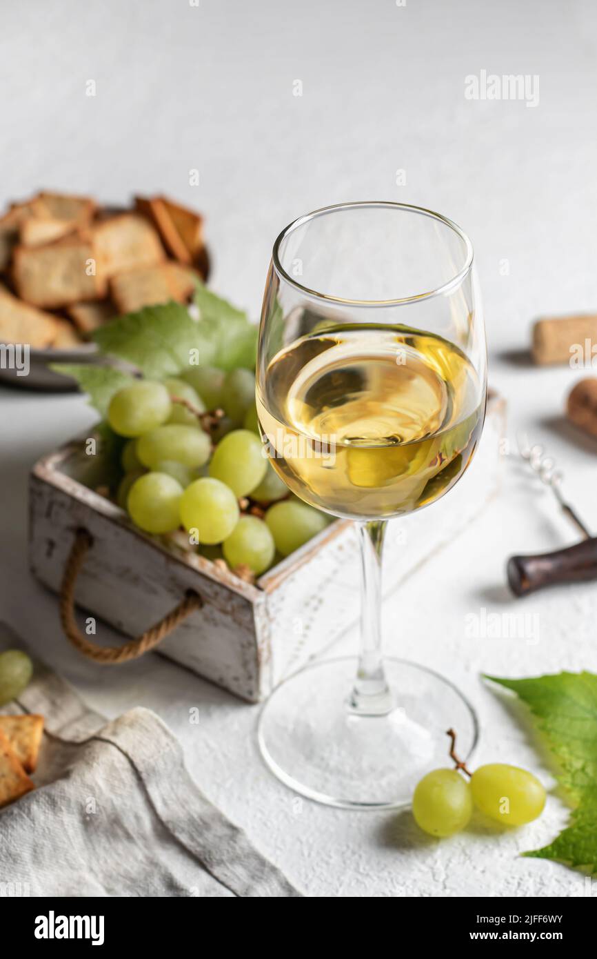 Verre de vin blanc avec raisins, corks et tire-bouchon et craquelins sur fond de table blanc Banque D'Images