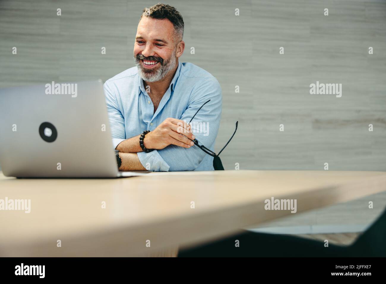 Heureux homme d'affaires mature assistant à une réunion en ligne avec ses associés. Entrepreneur enjoué ayant une vidéoconférence tout en travaillant à distance Banque D'Images