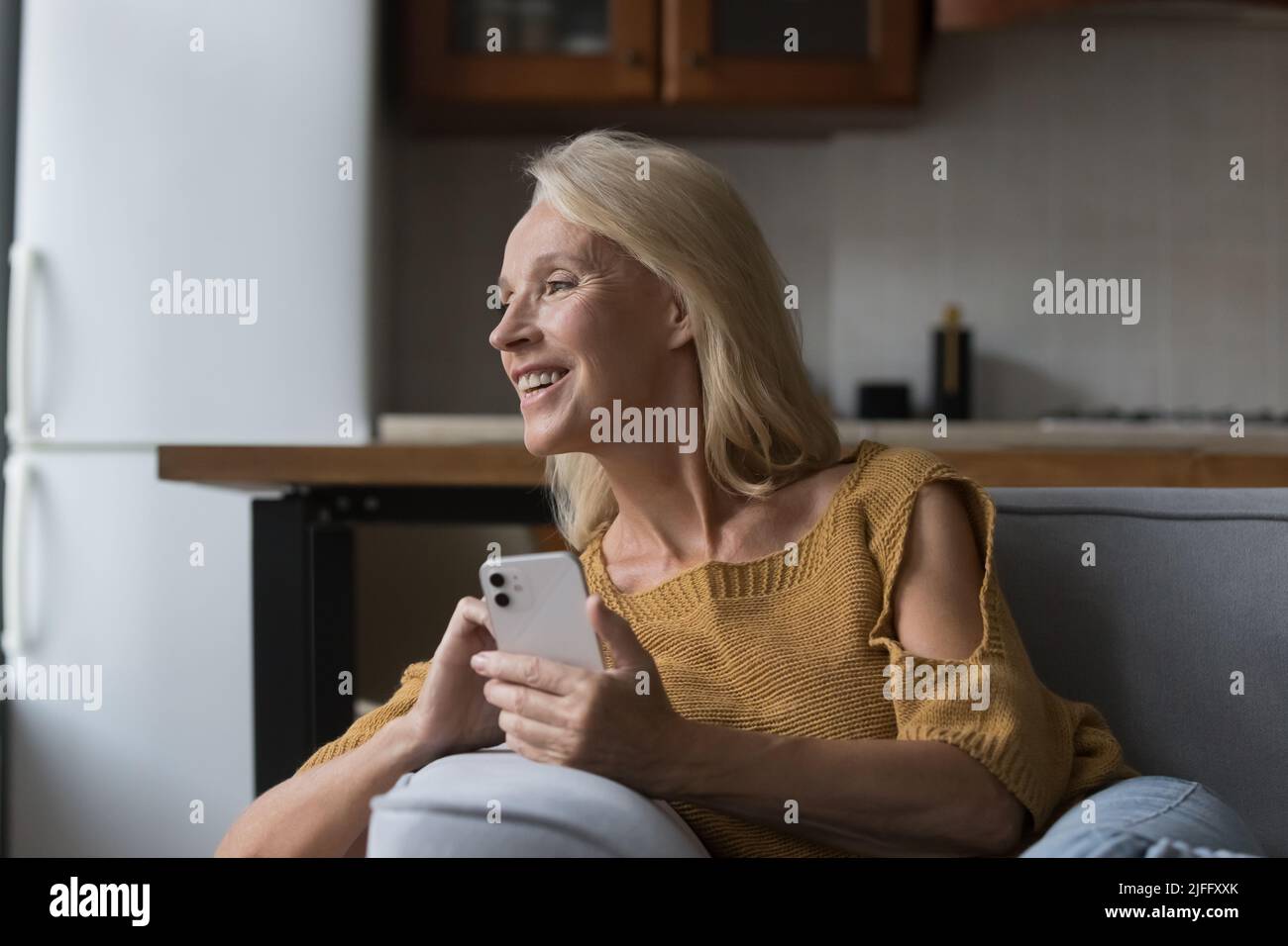 Une femme âgée rêveuse se détendre sur un canapé avec un téléphone portable Banque D'Images