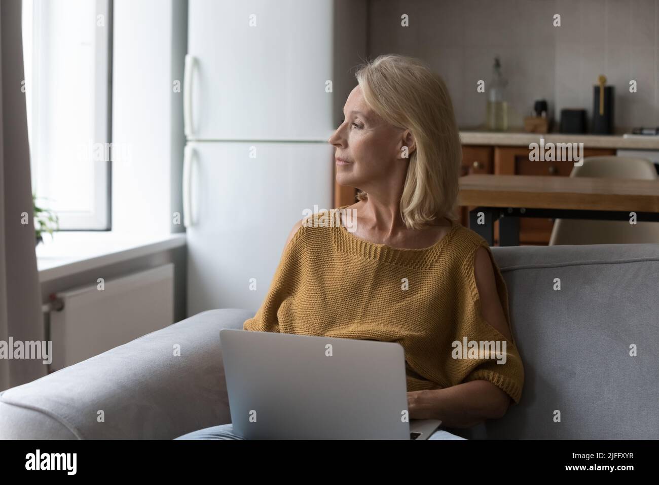 Une femme âgée pensive s'assoit sur un canapé avec un ordinateur portable Banque D'Images