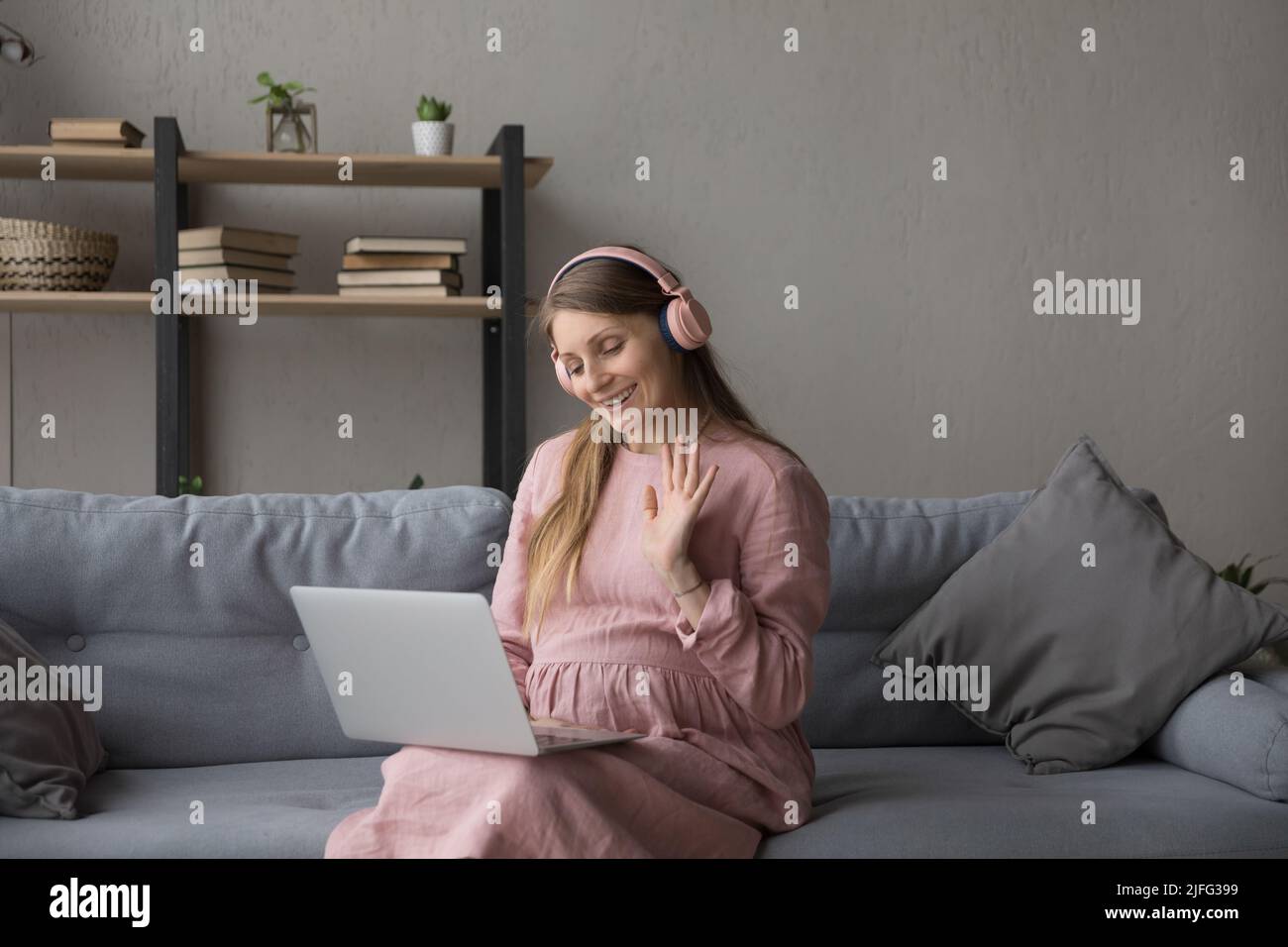 Une femme enceinte dans un casque utilise un ordinateur portable pour passer un appel vidéo Banque D'Images