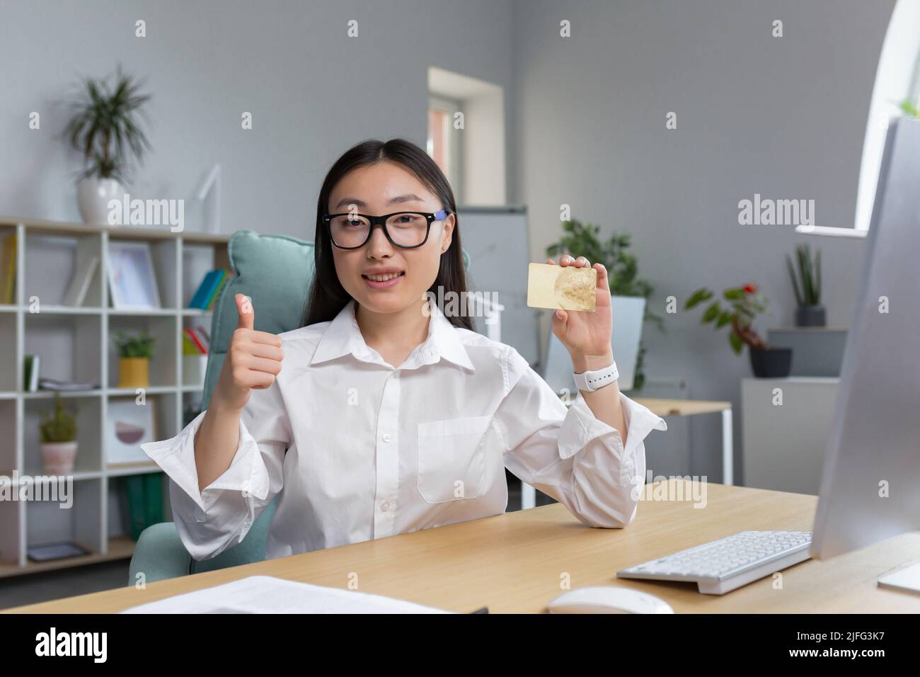 Belle femme d'affaires souriant et regardant l'appareil photo, femme asiatique offrant la carte bancaire aux clients, montrant les pouces avec la main, femme d'affaires travaillant dans le bureau. Banque D'Images