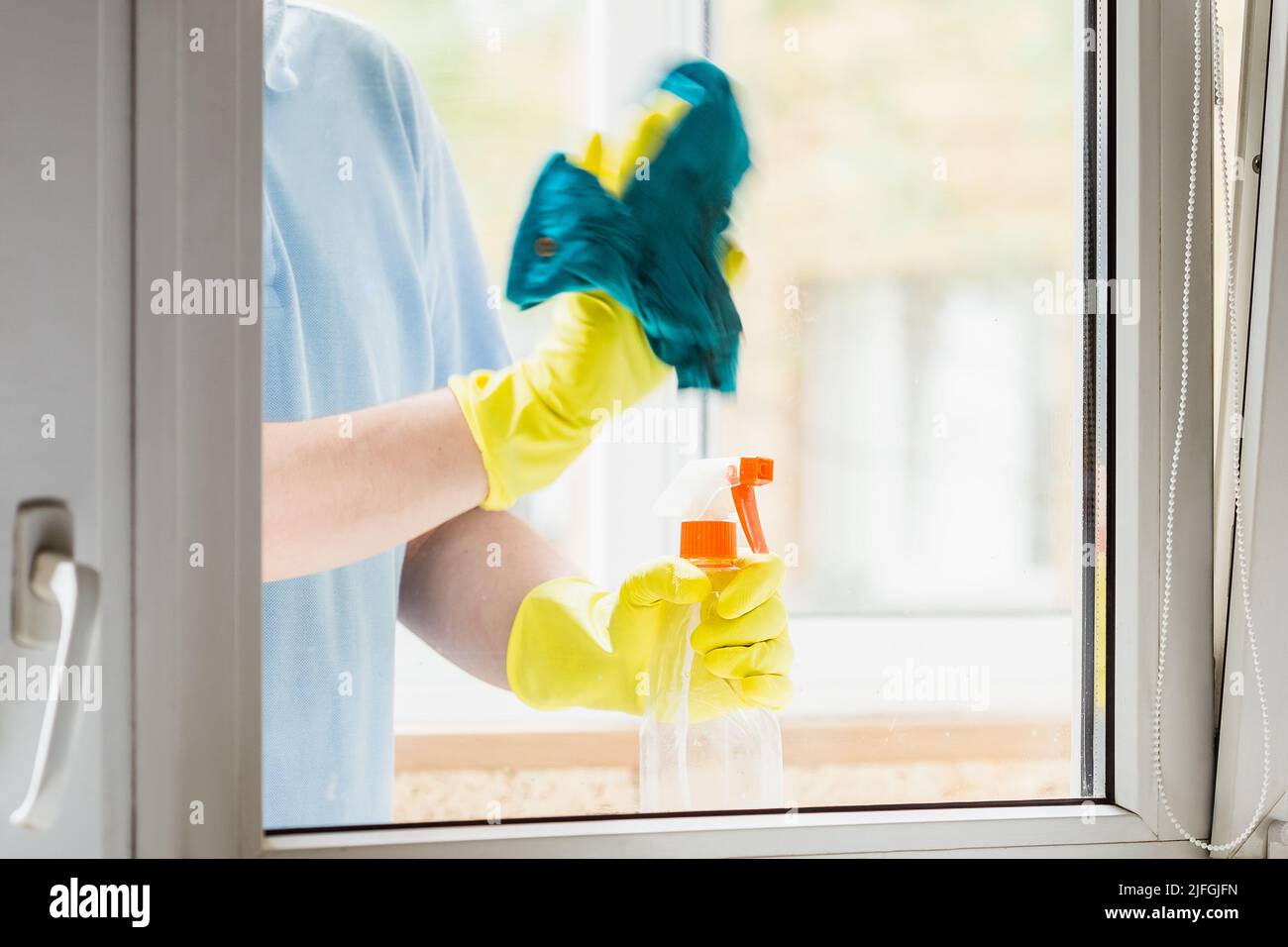 Homme dans des gants en caoutchouc jaune nettoyant les fenêtres à la maison. La main avec le chiffon est floue par le mouvement Banque D'Images