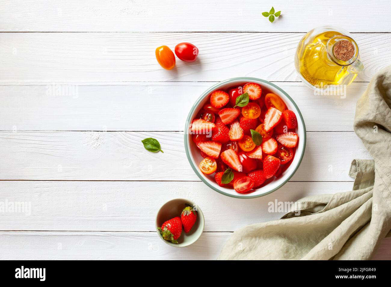 salade de tomates cerises et de fraises décorée de feuilles de basilic, fond en bois blanc, vue sur le dessus, espace copie Banque D'Images