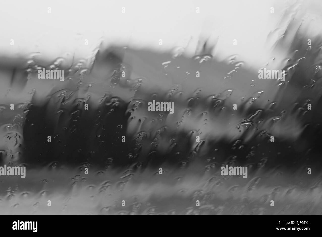 La vue d'une maison à travers la pluie qui s'étend sur le pare-brise en noir et blanc. Banque D'Images