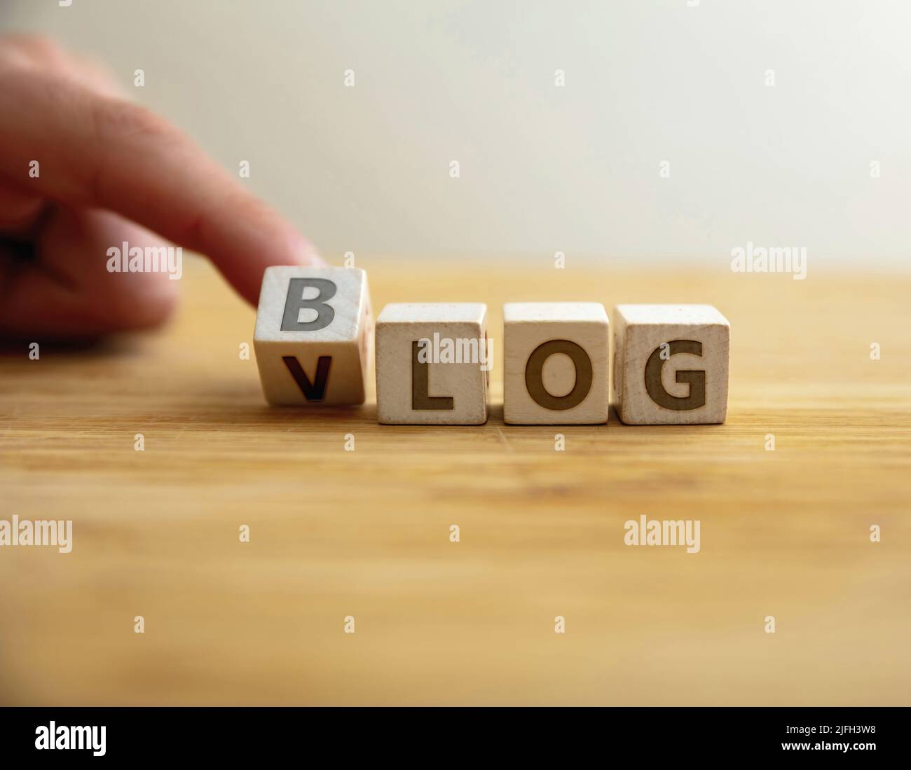 Blog VS vlog concept. Le doigt bascule la lettre à cube en bois changeant le mot blog à vlog. Message pour différence choix de promotion commerciale entre v Banque D'Images