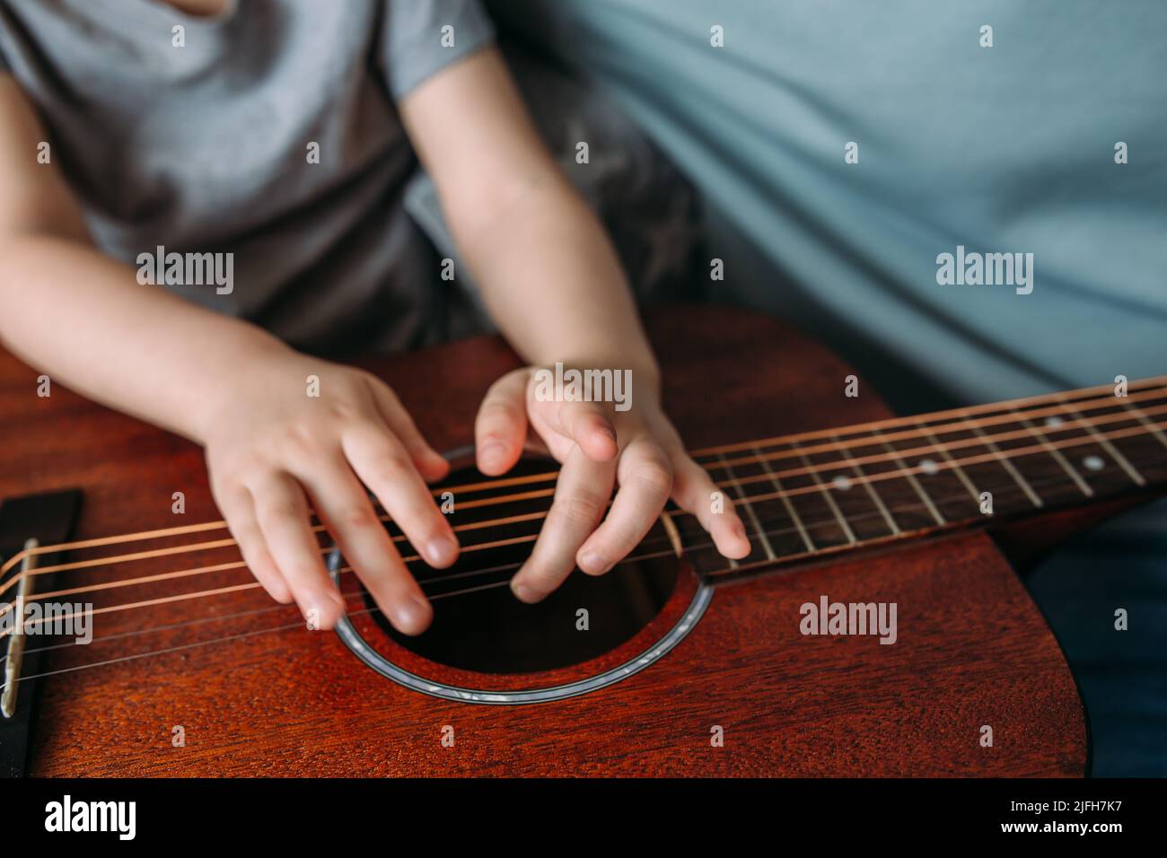 Un enfant mignon joue avec une grosse guitare acoustique à la maison Banque D'Images
